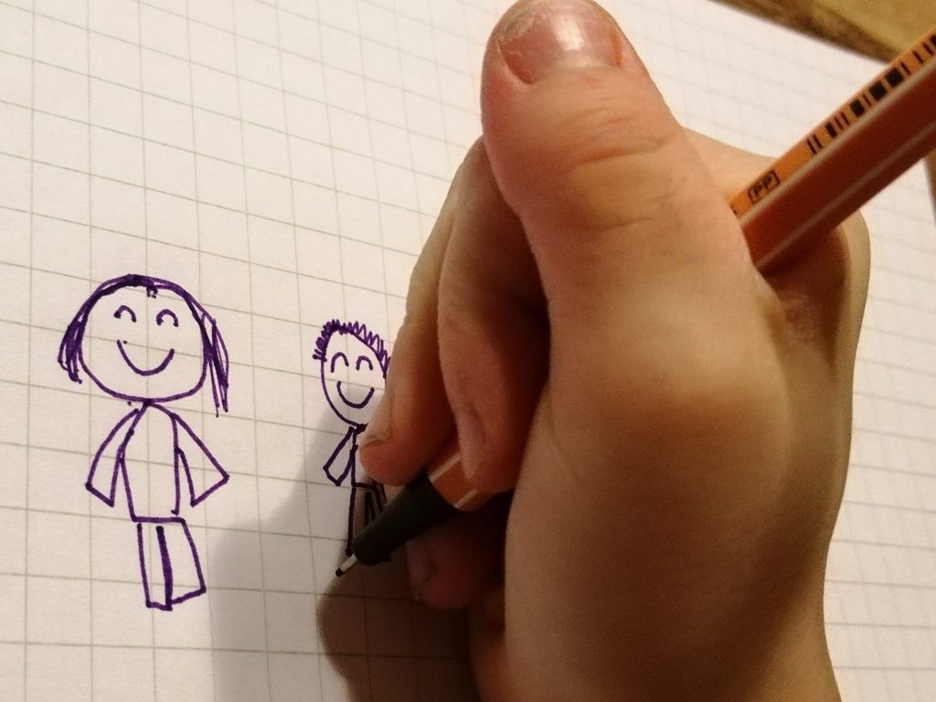 Lapsen käsi piirtää mustekynällä ruutupaperille kuvaa äidistä ja pojasta.