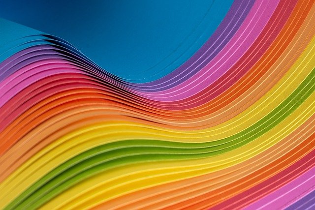 Aaltoilevaa paperia kaikissa sateenkaaren väreissä.