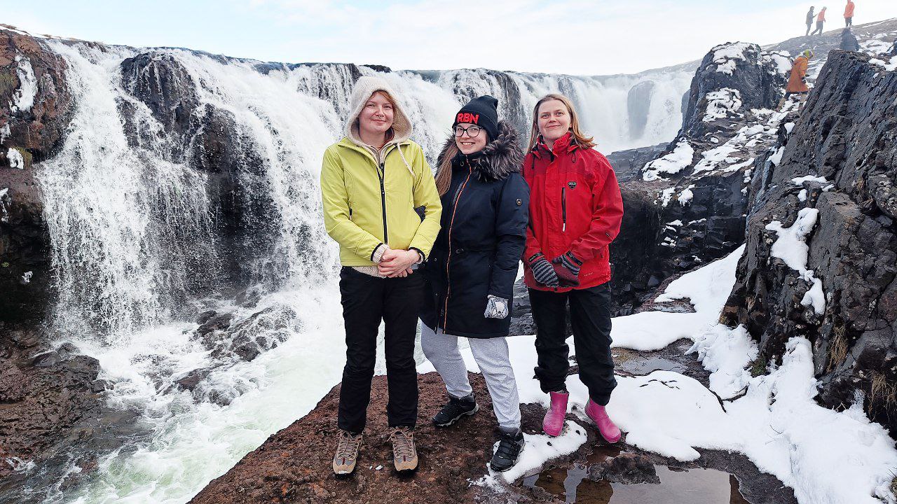 Three people pose in front of a waterfall.