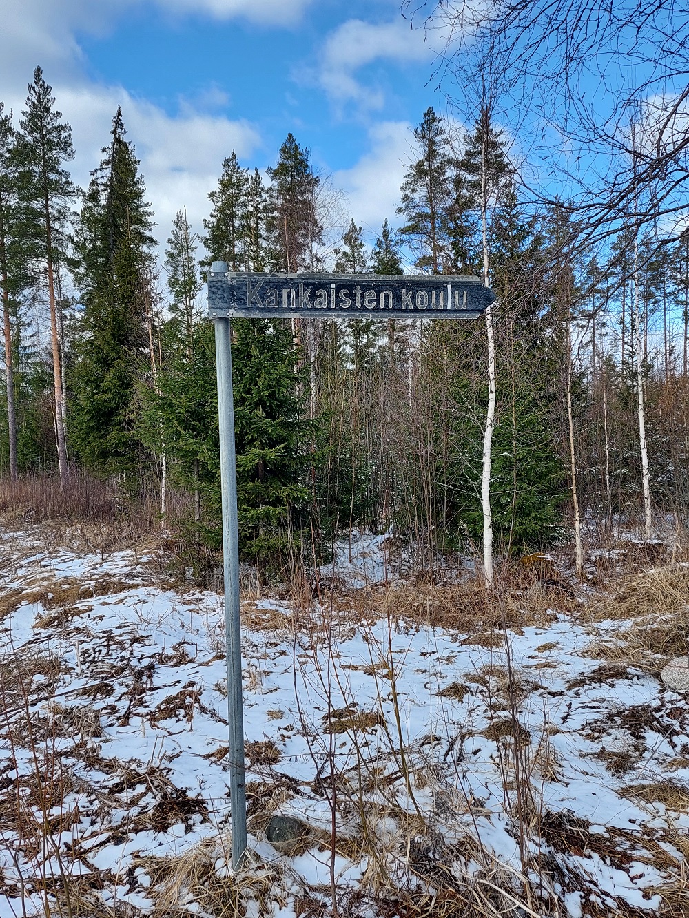 Kuvassa metsäinen ympäristö, vähän lunta ja tienviitta.